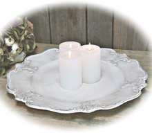 Antiikkivalkoinen patinoitu koristelautanen kynttilöiden alustana, kolme kynttilää kaikki valkoisia, pöydälle vanhanaikainen lautasen koristekuviointi heraldinen lilja La Petite Provence